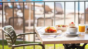 Una mesa de comedor con comida, un vaso de jugo de naranja y vista a una piscina.