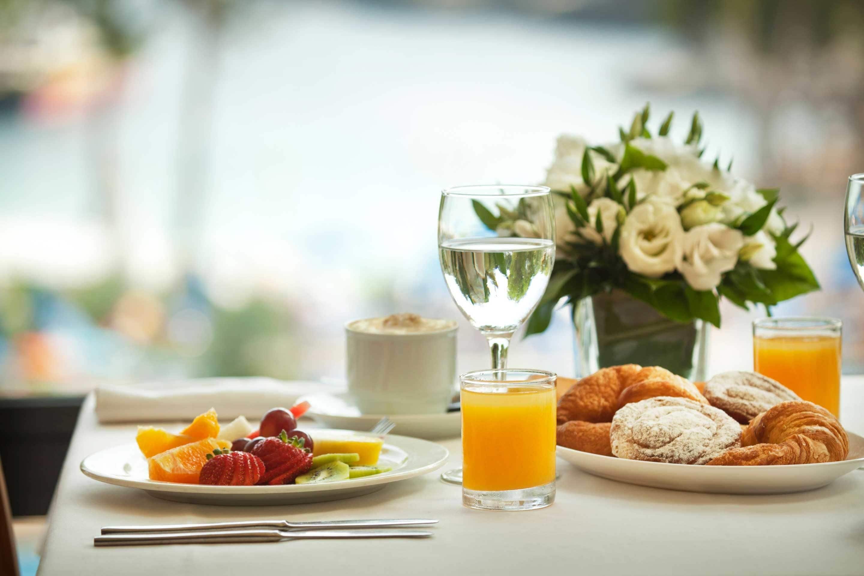 A breakfast table with croissants, fruit, a glass of orange juice, a glass of water, and a vase of flowers.