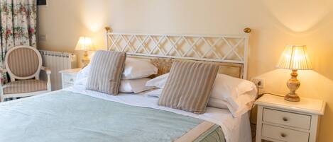 A neatly made bed with a striped headboard, two bedside lamps, a chair, and a small bedside table with a lamp.