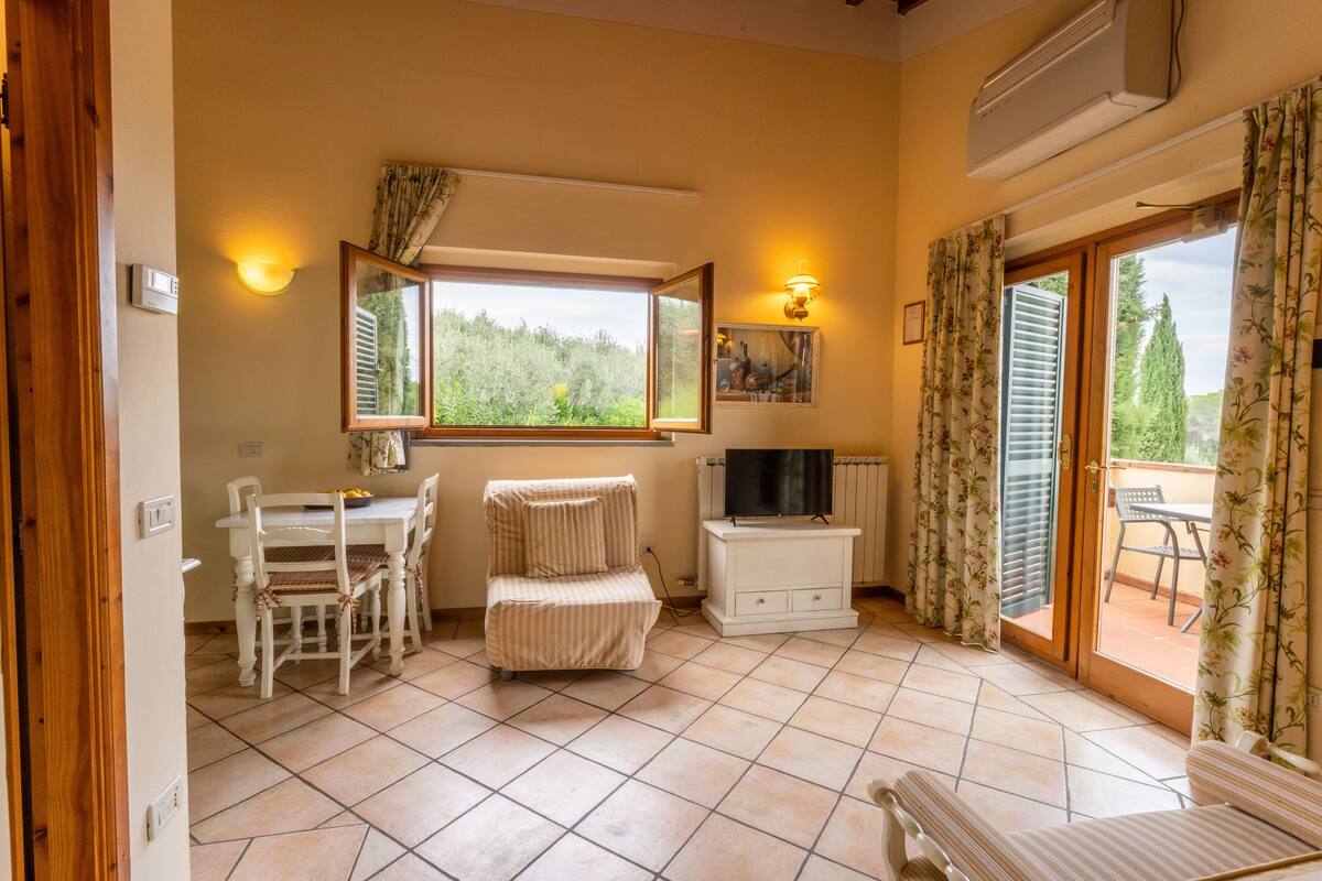 Une pièce comprenant une table à manger, des chaises, un banc rembourré, un téléviseur et une porte-fenêtre coulissante donnant sur un espace extérieur.