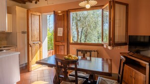 A kitchen with wooden cabinets, a dining table with chairs, a TV, and a window with a view of trees. - Agriturismo Vecchio Borgo di Inalbi (Impruneta)