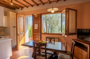Una cocina con armarios de madera, una mesa de comedor con sillas, un televisor y una ventana con vista a árboles.