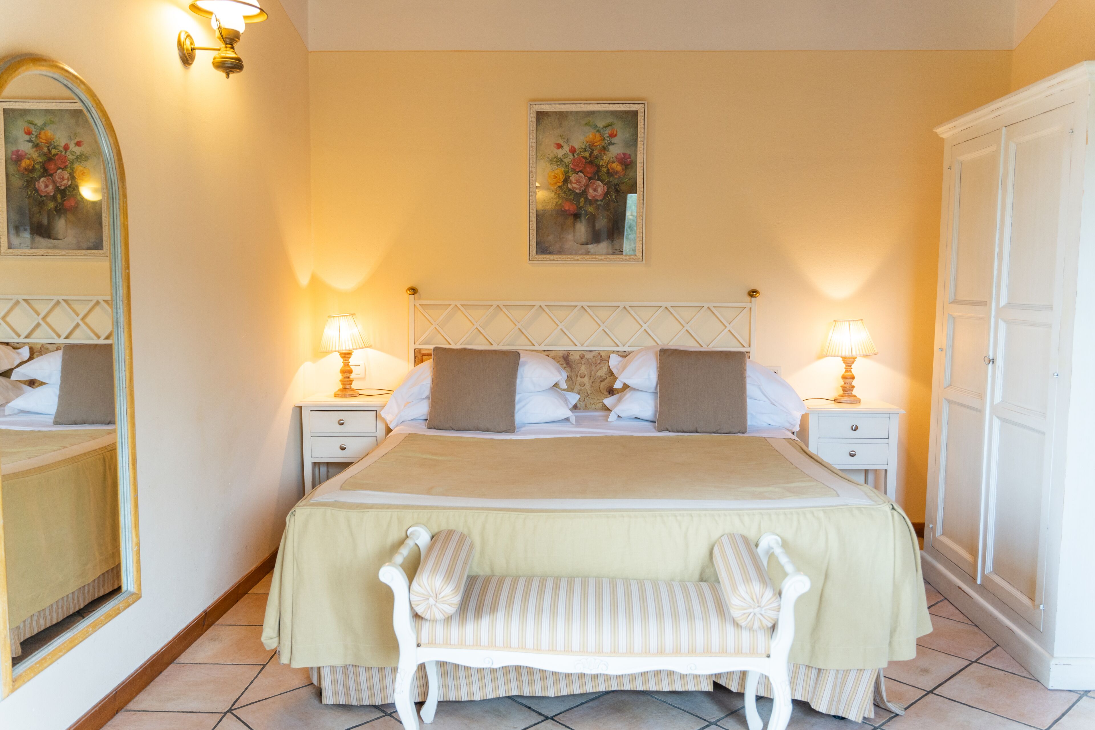 A neatly arranged bedroom with a large bed, two bedside tables with lamps, a bench, and a wardrobe.