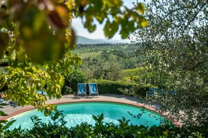 Piscina con sillones de descanso, rodeada de follaje y colinas al fondo.