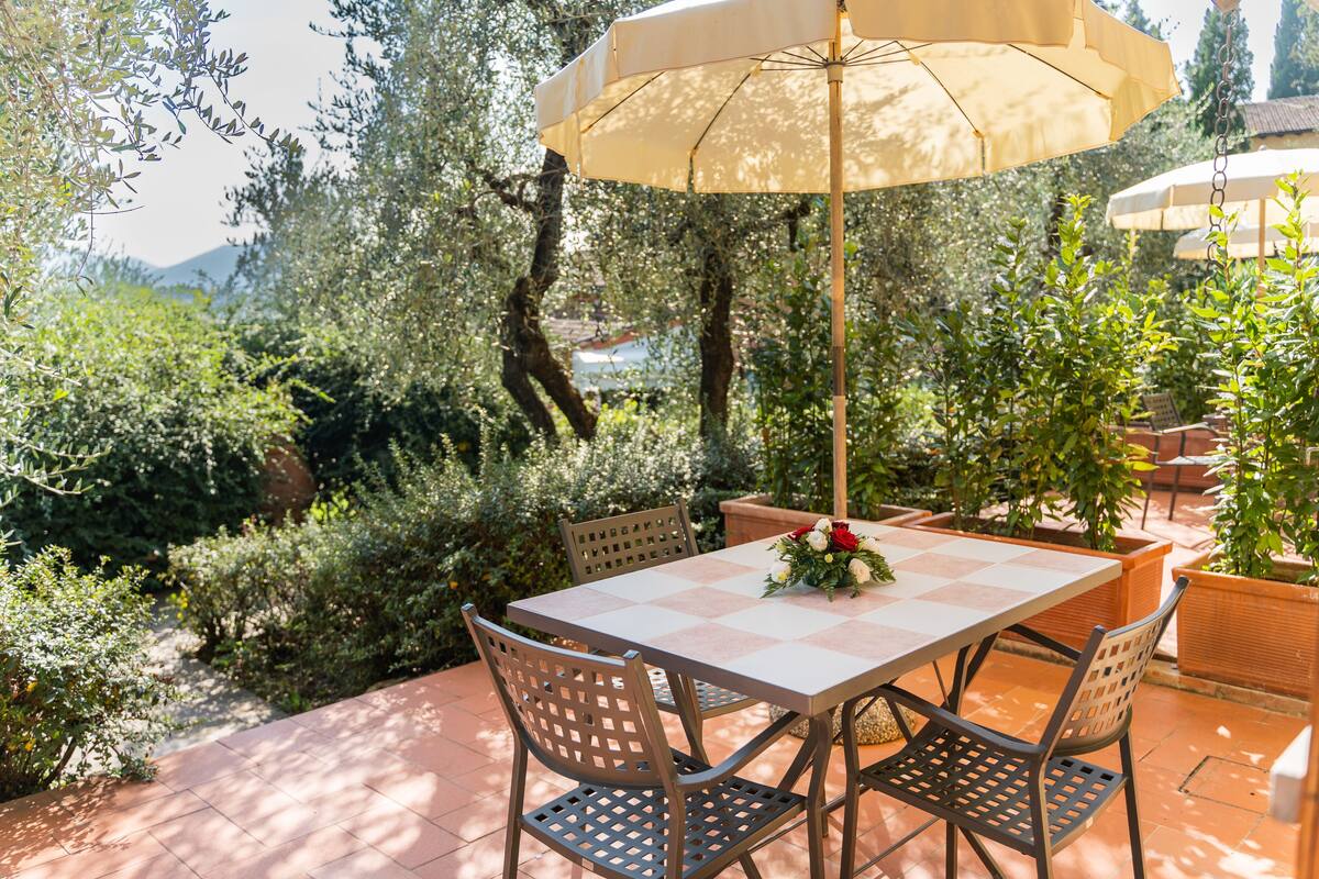 Une terrasse extérieure avec une table et des chaises, entourée de verdure et offrant une vue sur les montagnes.