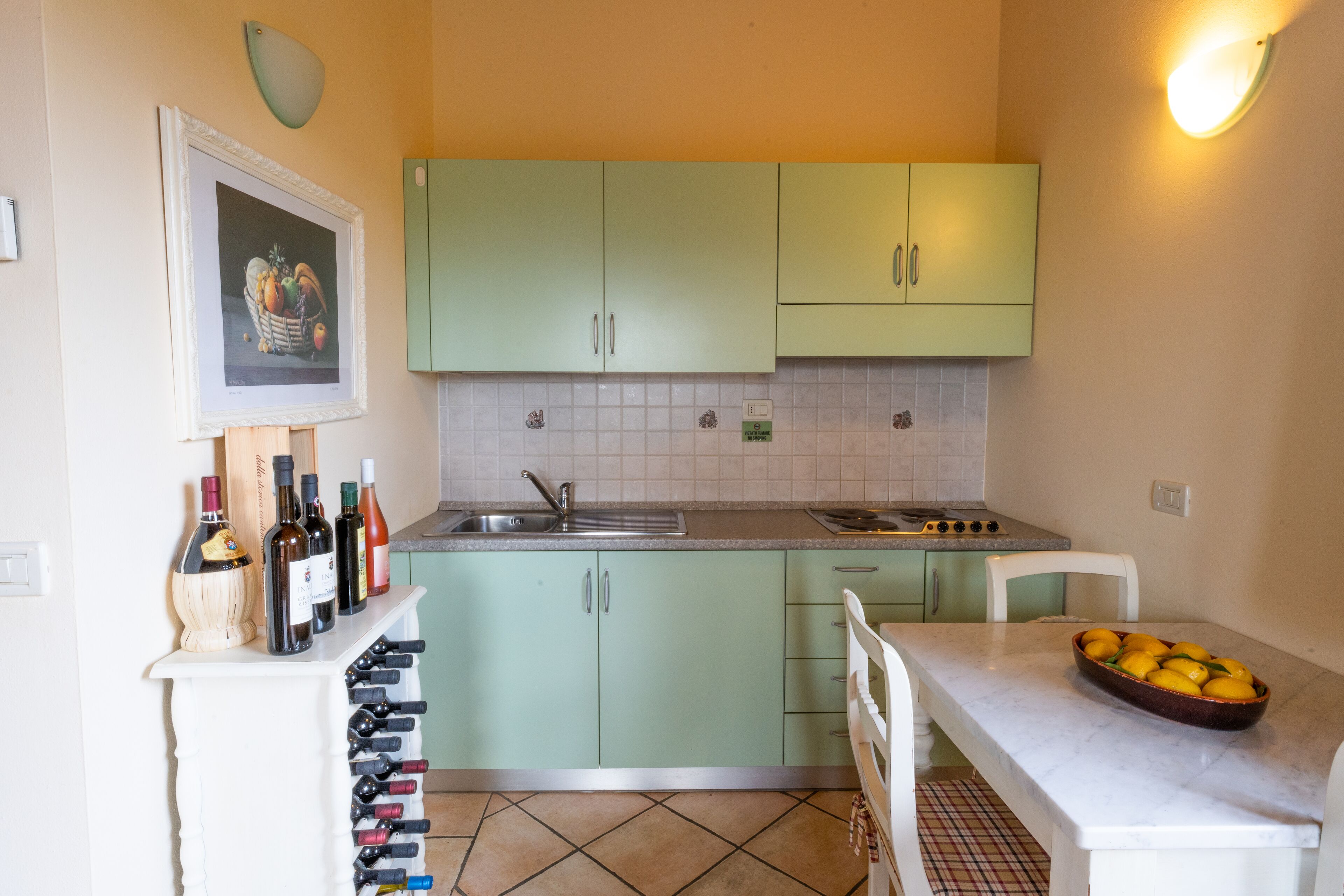 Une cuisine avec des meubles de rangement verts, un plan de travail blanc, un évier et un porte-bouteilles.