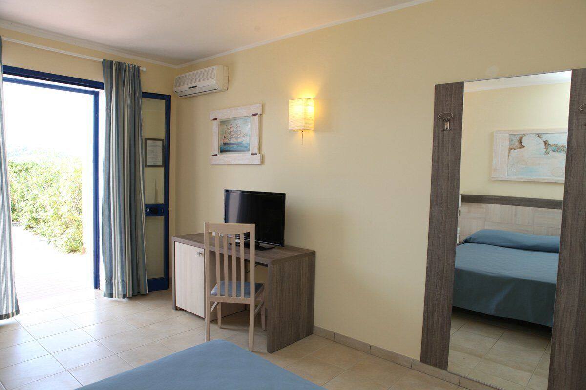 A room with a bed, a desk with a chair, a television, and a wall-mounted light.