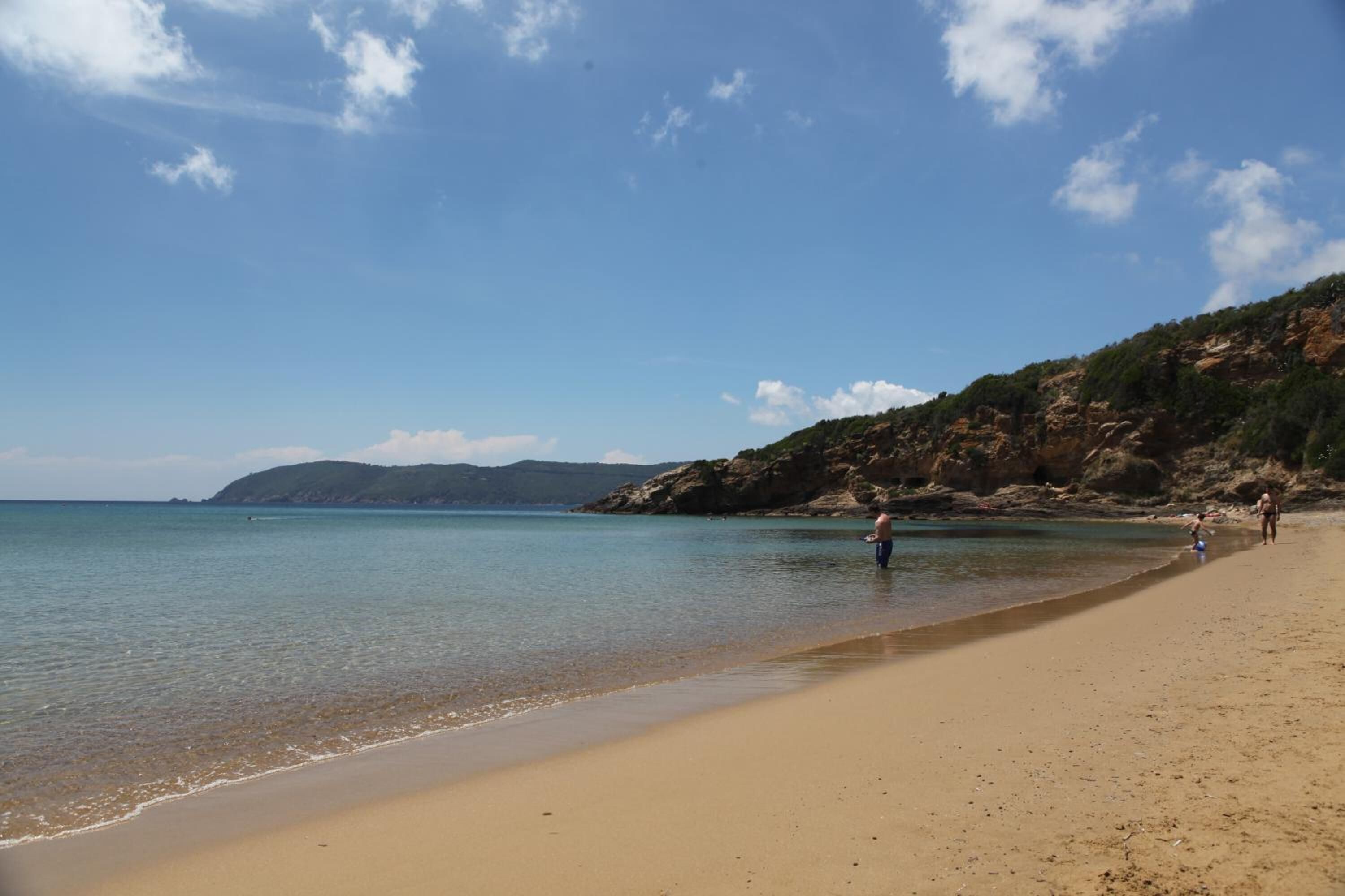 Egy tiszta vizű strand, homokos parttal, és a háttérben sziklás dombokkal.