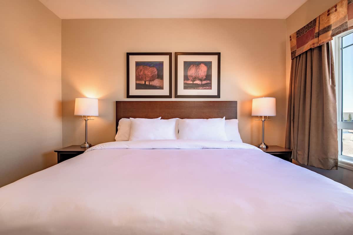 Una habitación de hotel con una cama grande, dos lámparas de noche y dos cuadros en la pared.