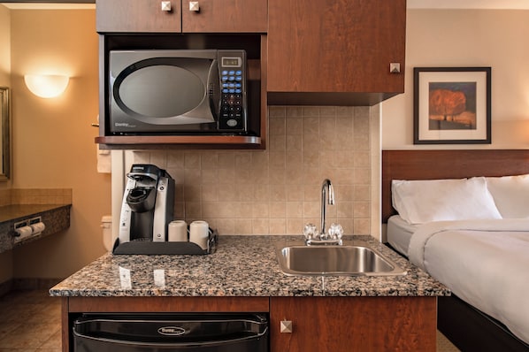 A compact hotel kitchen with a microwave, coffee maker, and sink. - Canalta Hotel High River (High River)