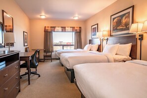 Ein Hotelzimmer mit zwei Betten, einem Schreibtisch, einem Stuhl, einer Kommode und einem Fenster mit Vorhängen.