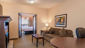 A hotel room with a bed, a sofa, a coffee table, a desk, and a painting on the wall. - Canalta Hotel High River (High River)