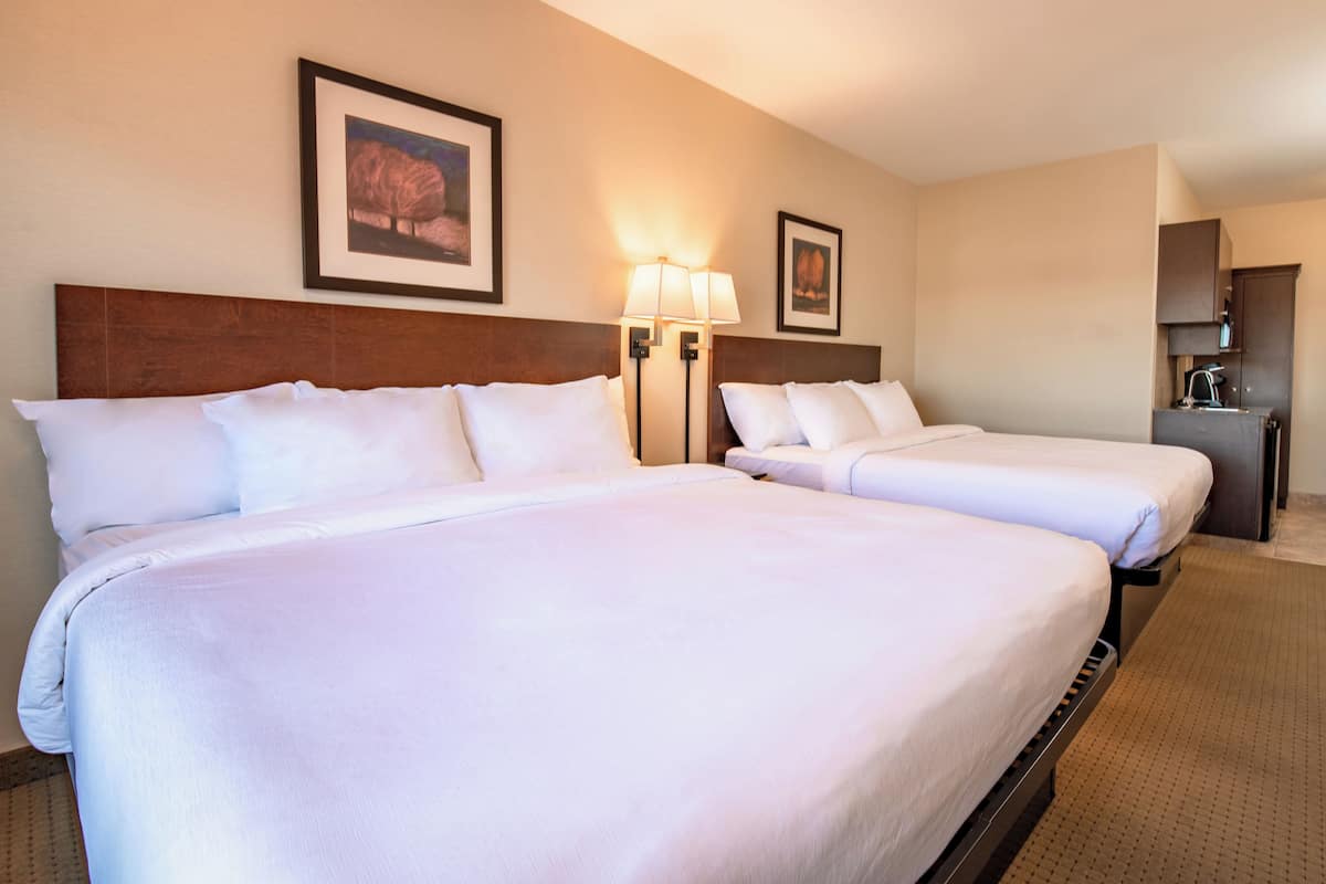Habitación de hotel con dos camas, cabecero de madera, lámparas de pared y cuadros enmarcados.