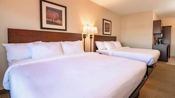 A hotel room with two beds, a wooden headboard, wall-mounted lamps, and framed pictures.