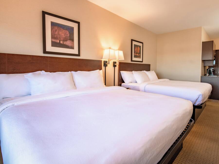 A hotel room with two beds, a wooden headboard, wall-mounted lamps, and framed pictures.