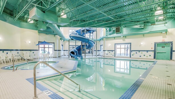 An indoor swimming pool with a blue spiral slide, tiled walls, and a clear pool area. - Canalta Hotel High River (High River)