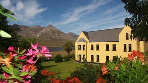 A yellow building with a symmetrical facade, a well-maintained lawn, and mountains in the background.