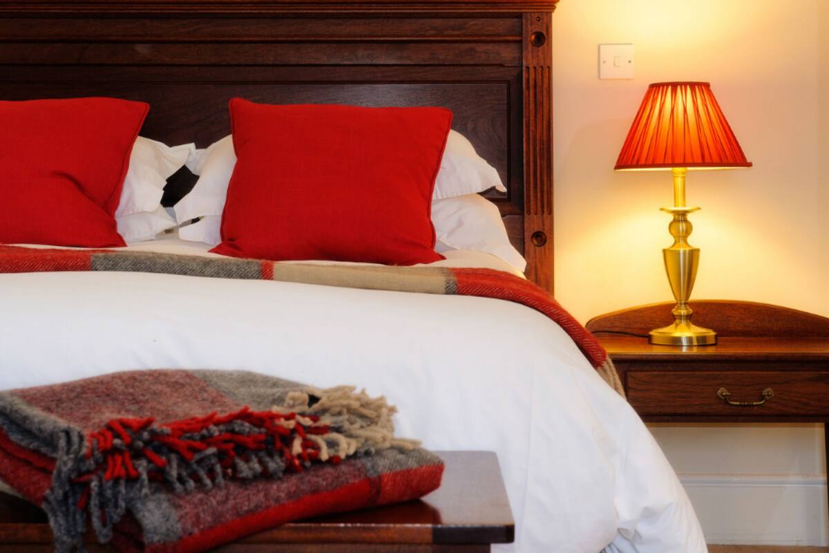 A neatly made bed with red and white bedding, a wooden headboard, and a bedside table with a lamp.