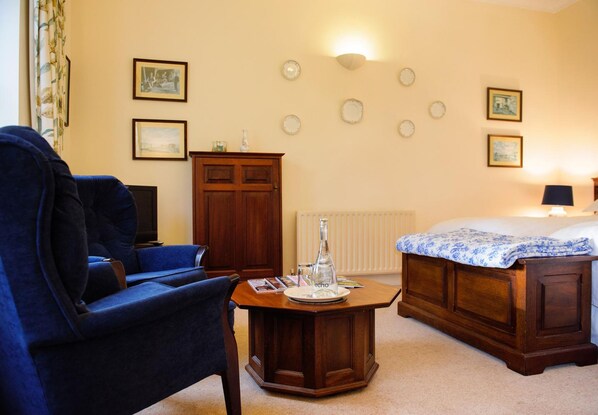 Una habitación de hotel con una cama, un sillón azul, un armario de madera, una mesa redonda con una botella y luces fijadas a la pared.