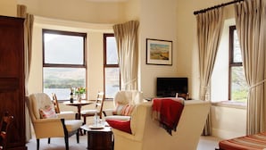 A living room with a sofa, armchairs, a TV, and large windows with curtains.