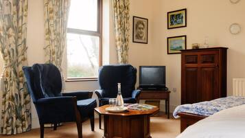 A hotel room with two armchairs, a wooden coffee table, a television, a cabinet, and a bed.