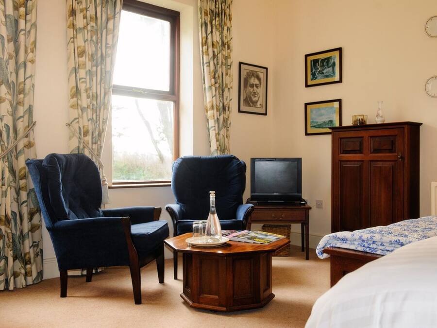 A hotel room with two armchairs, a wooden coffee table, a television, a cabinet, and a bed.