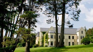 A large, multi-story building with a symmetrical facade, surrounded by a well-maintained lawn and tall trees.