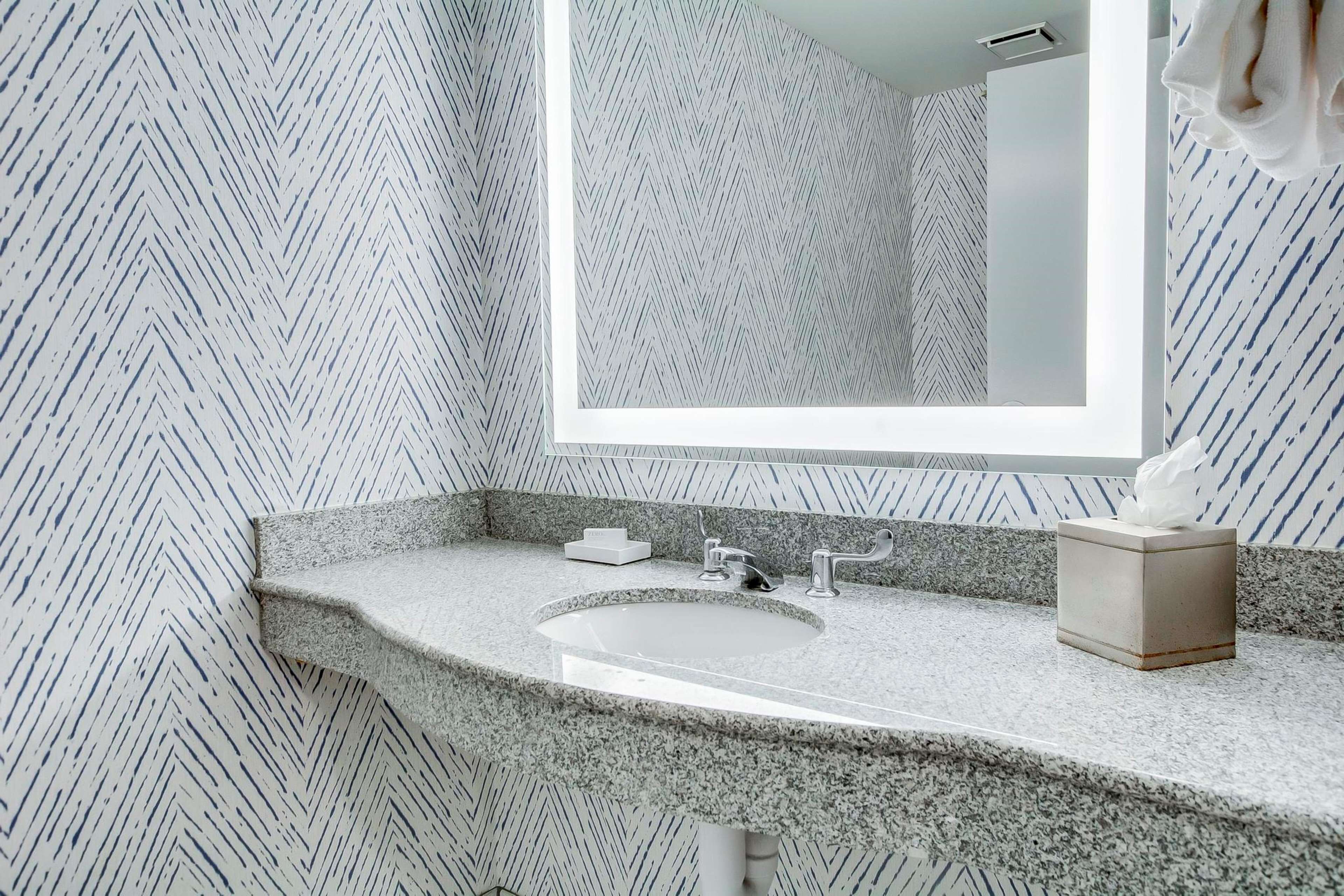 A bathroom with a granite countertop, a sink, a mirror, and a towel dispenser.