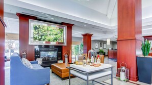A modern lobby with a blue sofa, a coffee table, a TV mounted on a wooden pillar, and a reception desk.