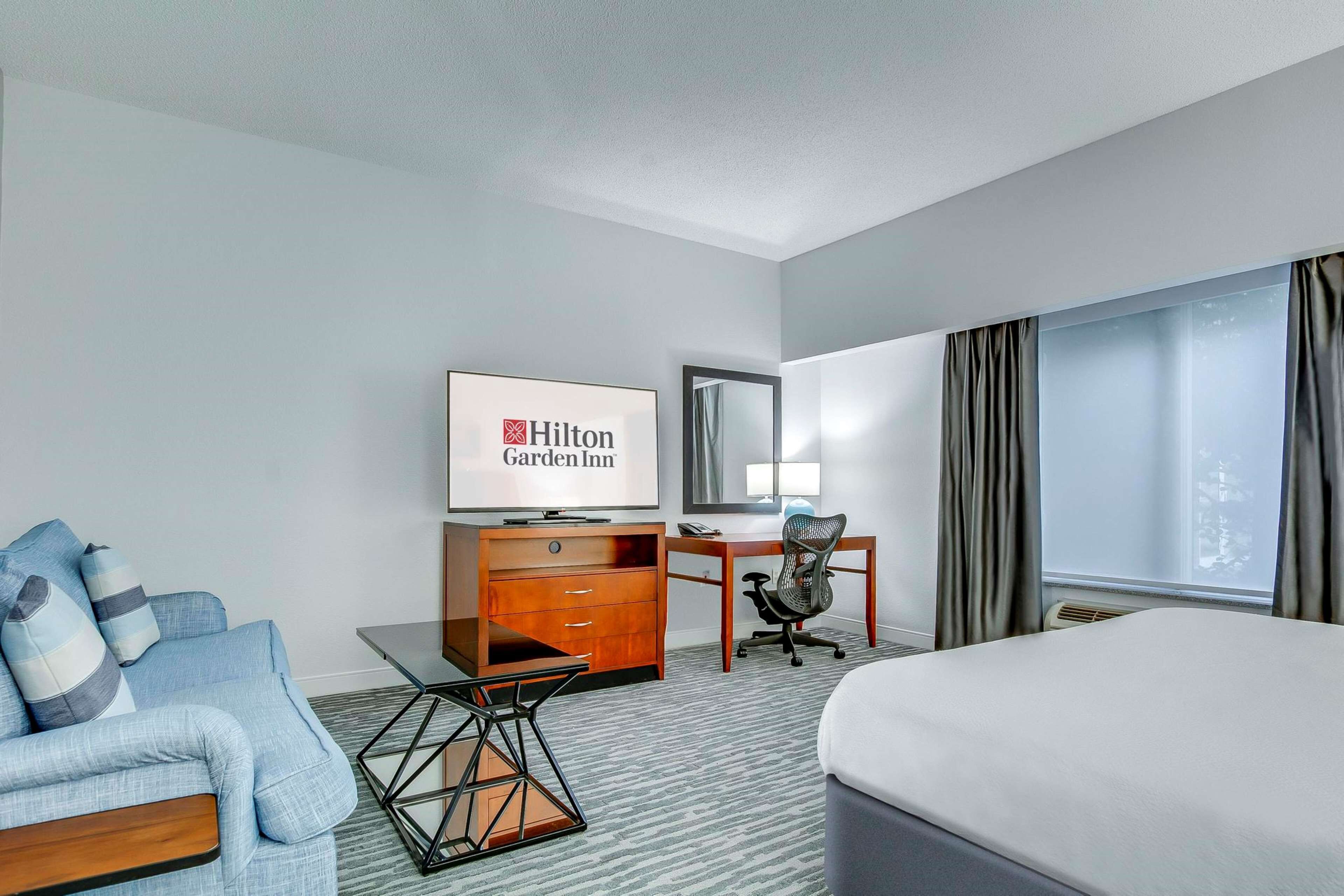 Une chambre d’hôtel avec un lit, un bureau, une chaise, une télévision et un canapé.