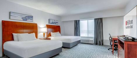 Quarto de hotel com duas camas, uma escrivaninha e uma janela grande com cortinas.