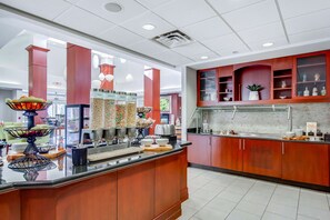 A modern hotel lobby with a buffet area, wooden cabinets, and a bright ceiling. - Hilton Garden Inn Louisville/Northeast (Louisville)