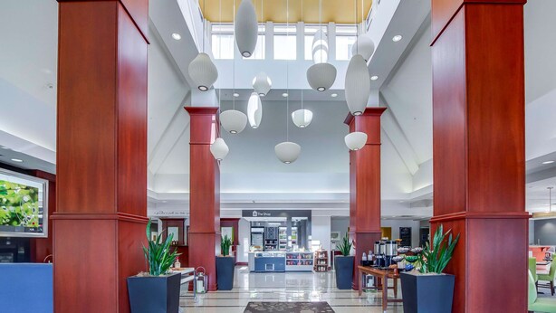 A spacious lobby with a central reception desk, a coffee station, and a shop in the background.