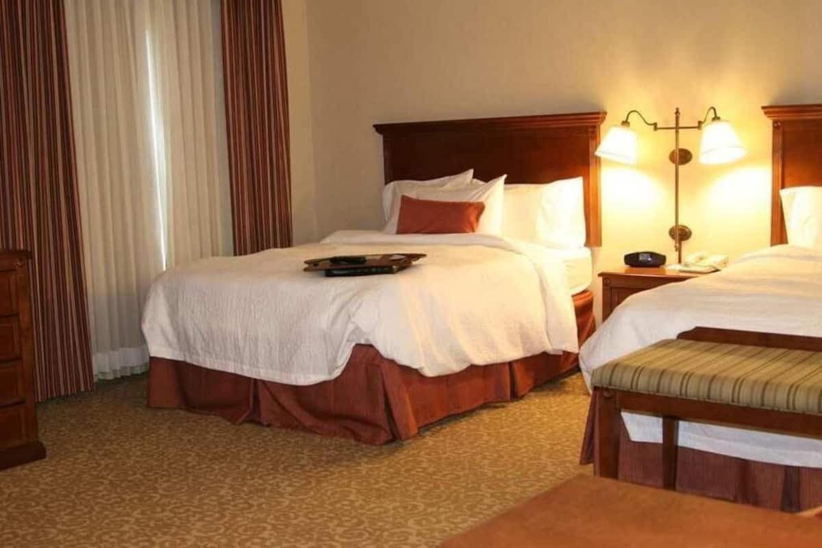 A hotel room with two beds, a bedside table with lamps, a dresser, and a patterned carpet.