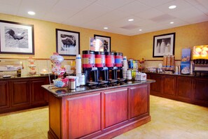 A hotel lobby with a coffee station, framed pictures on the walls, and a tiled floor.