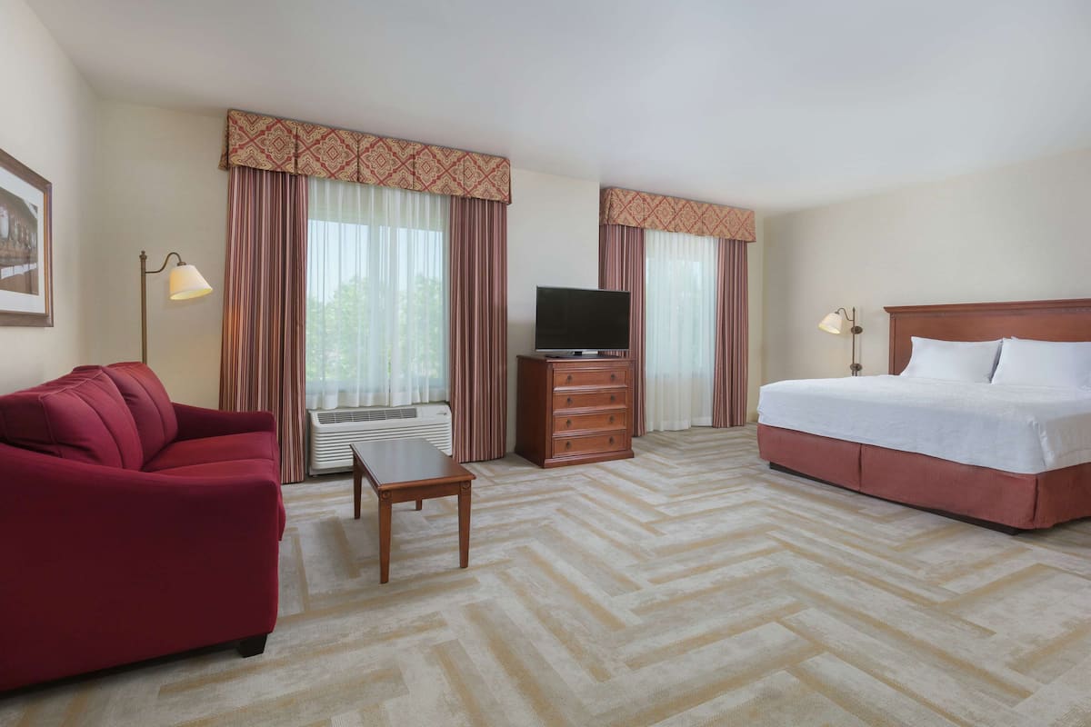 A hotel room with a bed, a red sofa, a TV on a wooden cabinet, and a desk.