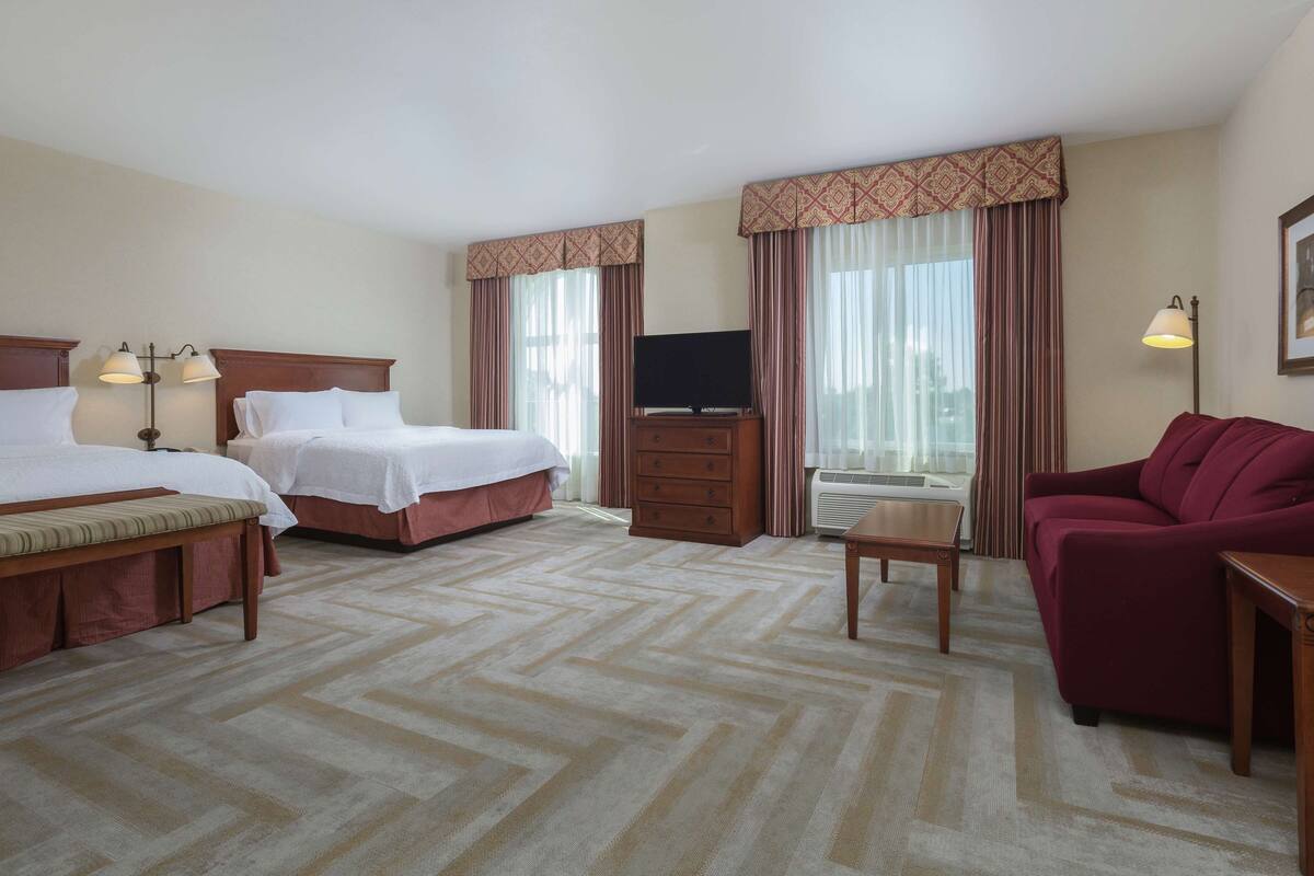 A hotel room with two beds, a television, a desk, a chair, and a couch.