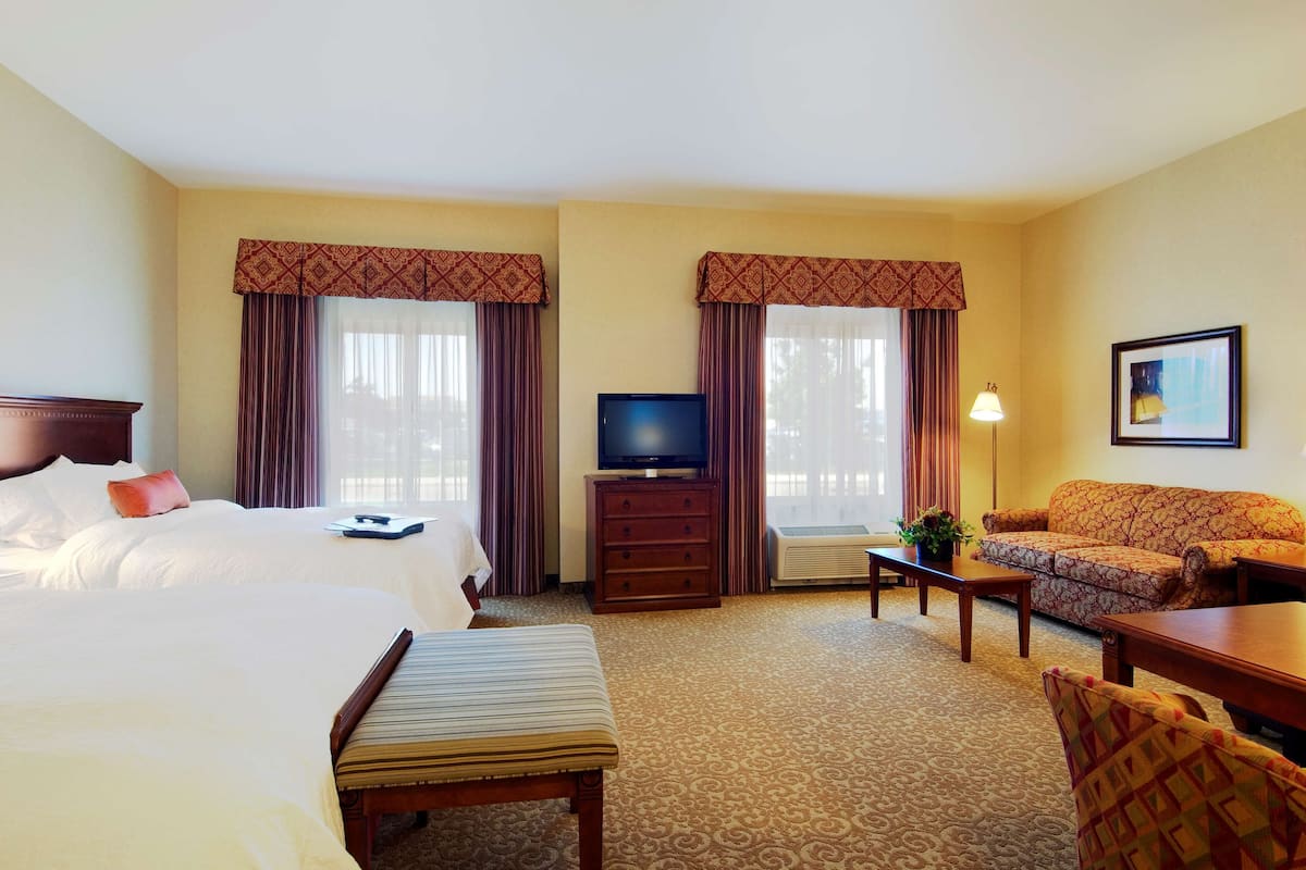 A hotel room with two beds, a television, a sofa, and a desk.