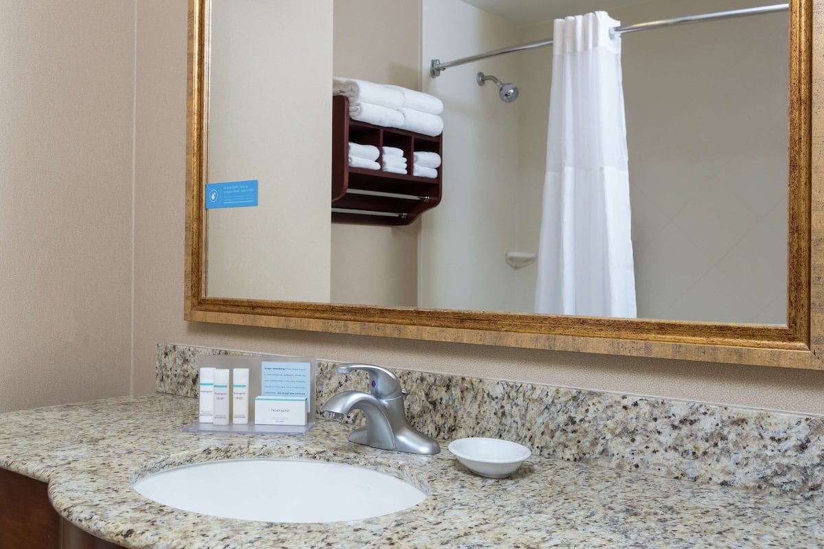 A bathroom with a granite countertop, a white sink, a silver faucet, and a mirror with a gold frame.