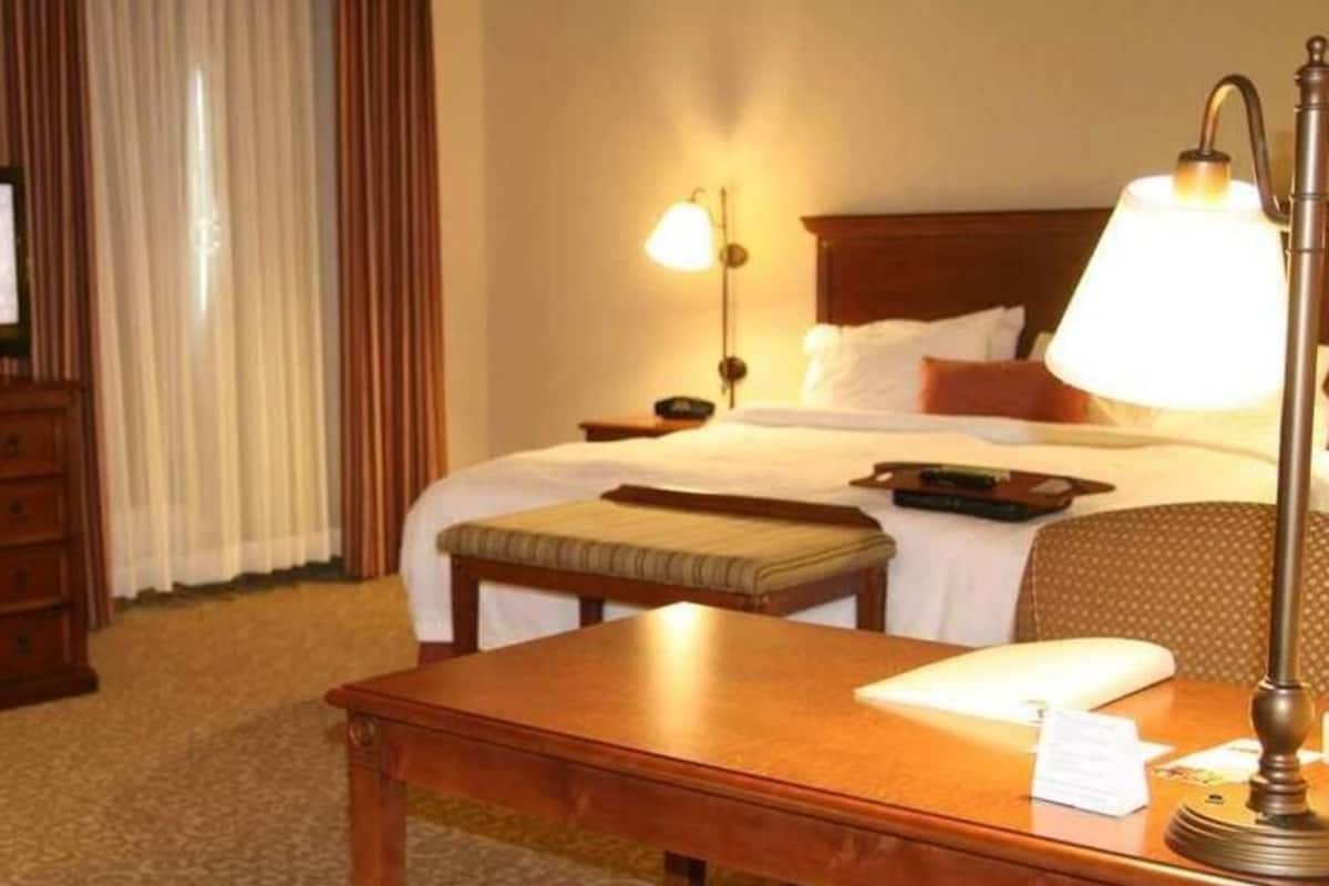 A hotel room with a bed, bedside lamps, a wooden table, a chair, and a desk with a lamp.