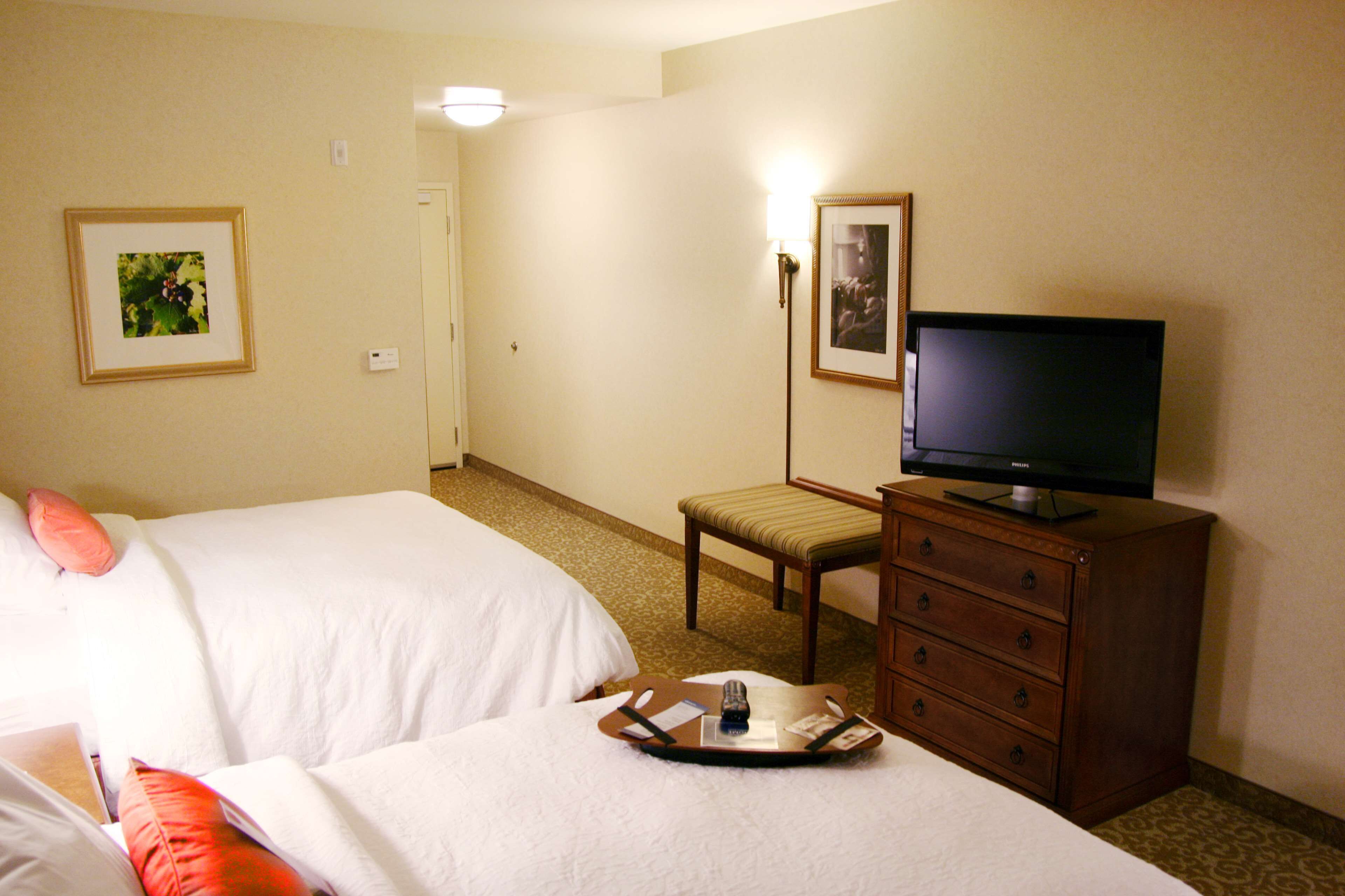 Habitación de hotel con dos camas, televisión, cómoda y una mesita con objetos encima.