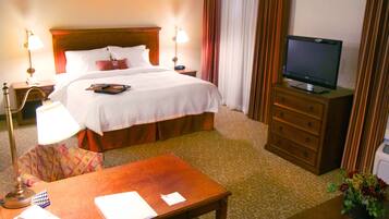 A hotel room with a bed, bedside tables, a desk, a television, and a small table with a flower vase.