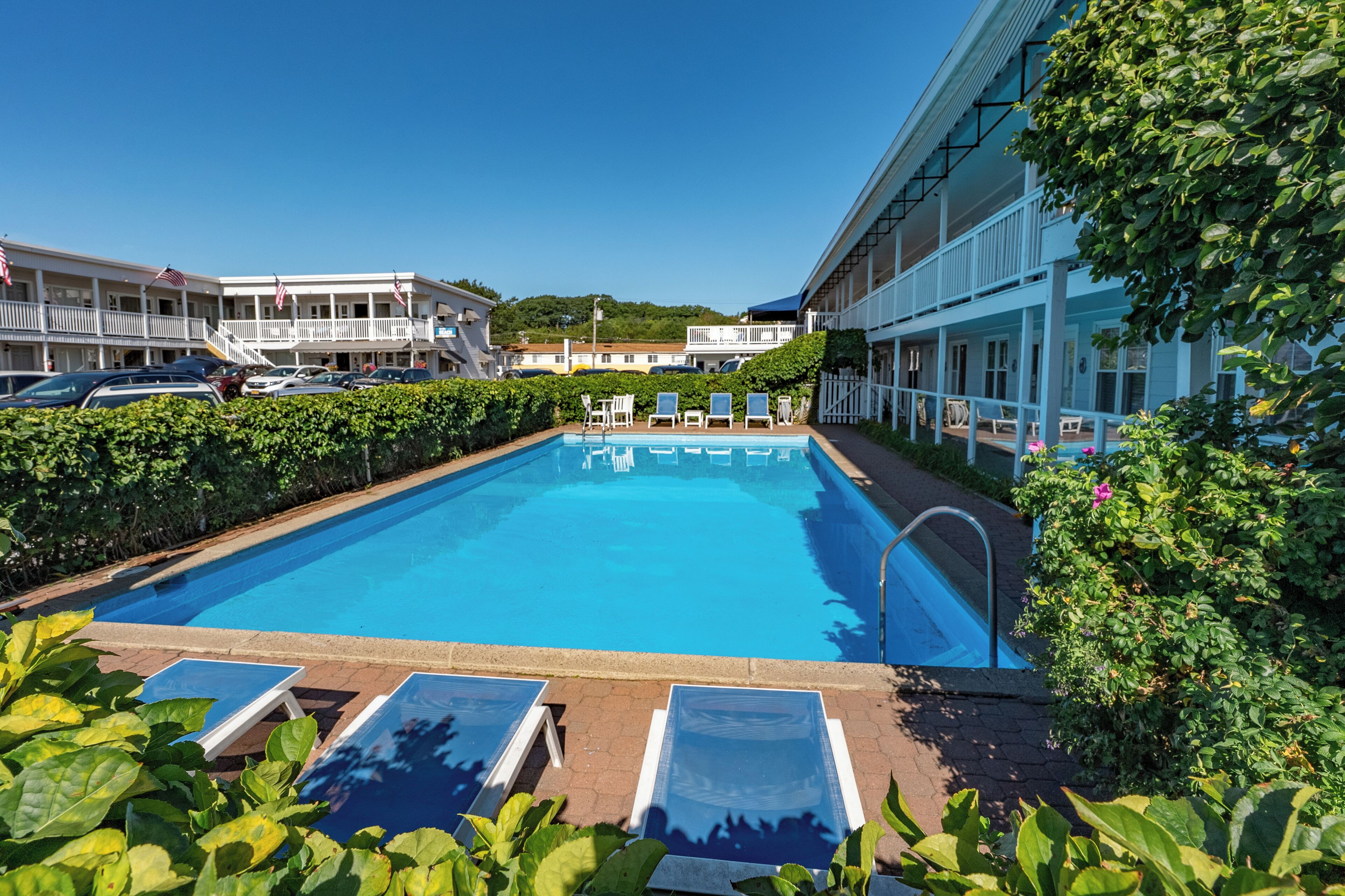 A swimming pool with lounge chairs, surrounded by greenery and a building with a balcony.