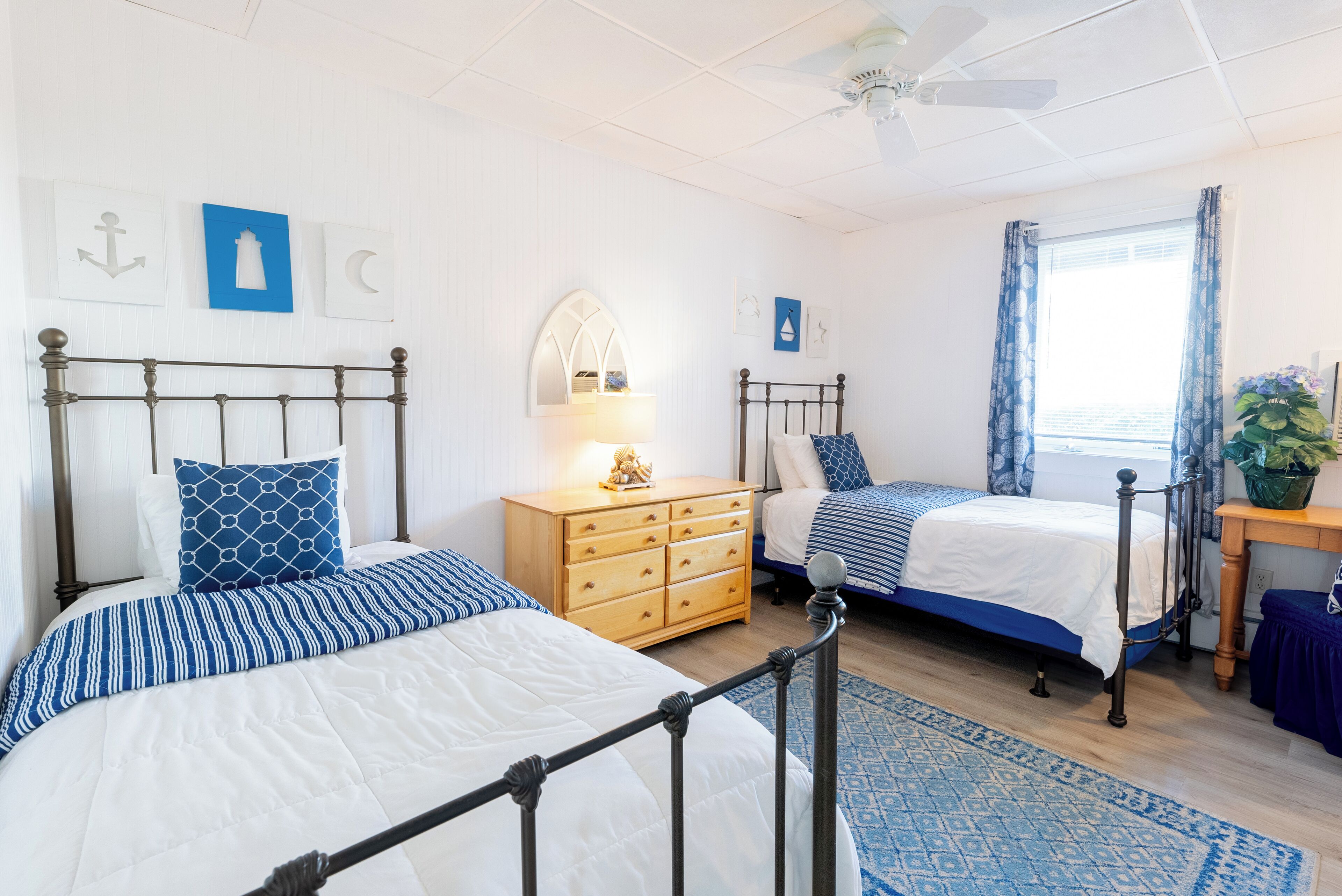 A bedroom with two beds, a wooden dresser, a mirror, and a window with curtains.