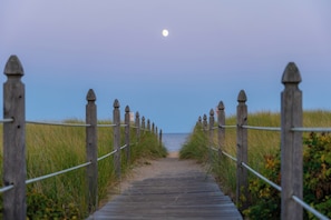 A wooden boardwalk leading to the beach with a moon in the sky.