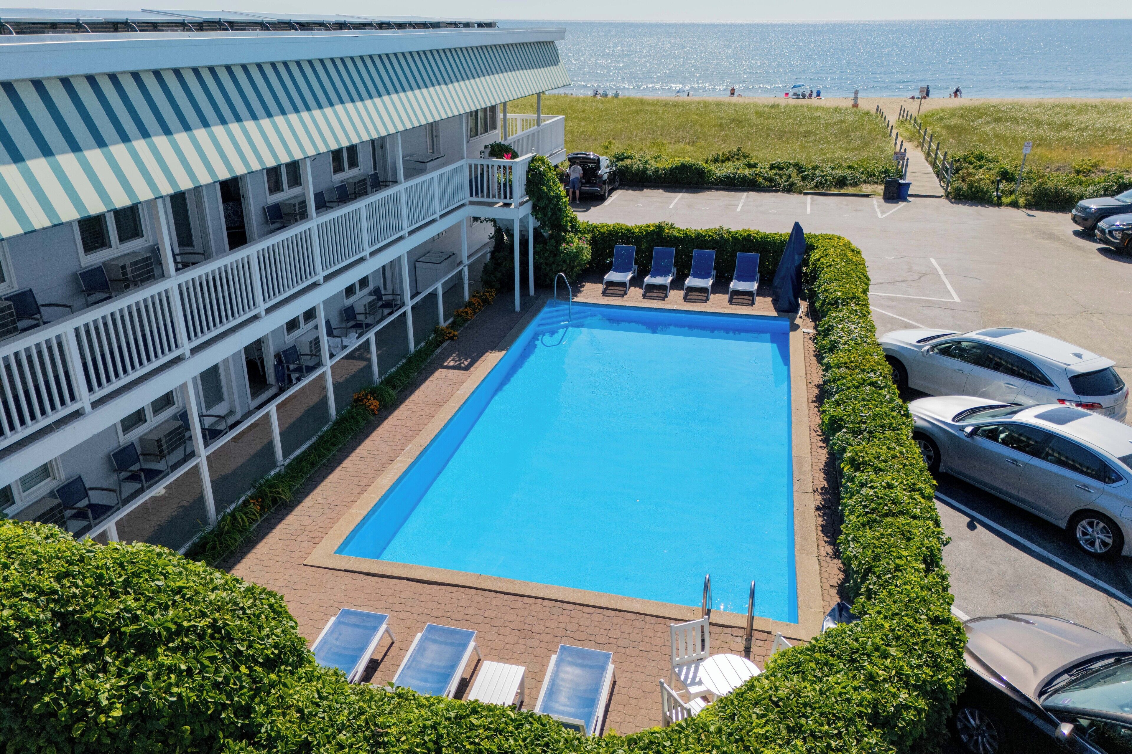 A hotel with a swimming pool, lounge chairs, and a view of the beach.