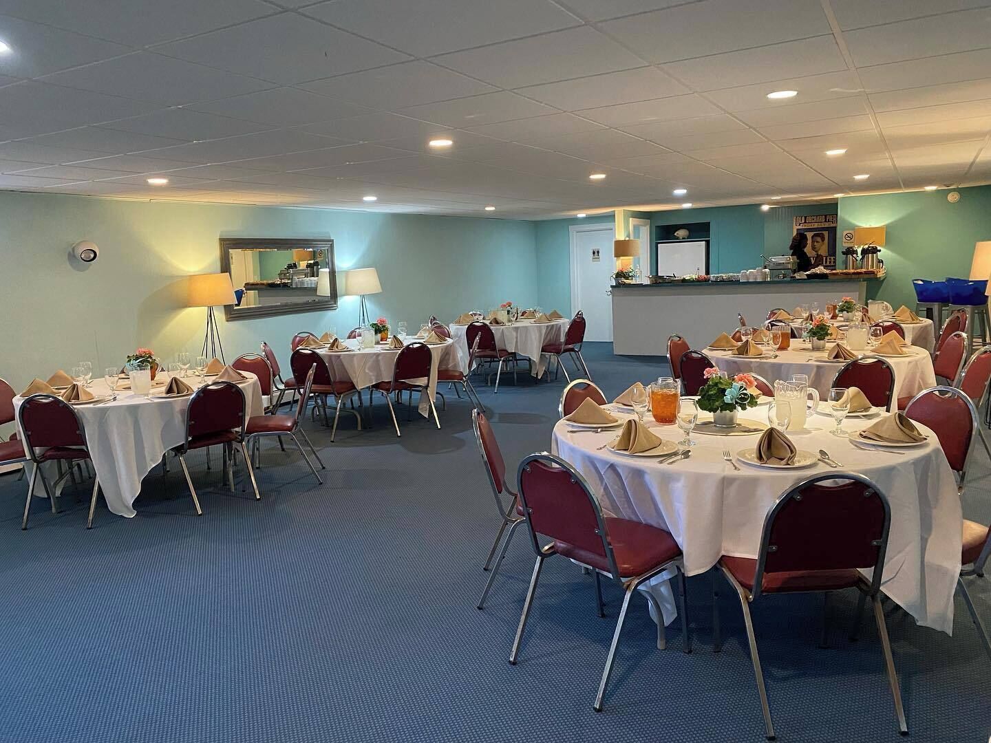 Een vergaderzaal met meerdere ronde tafels, rode stoelen en witte tafelkleden.