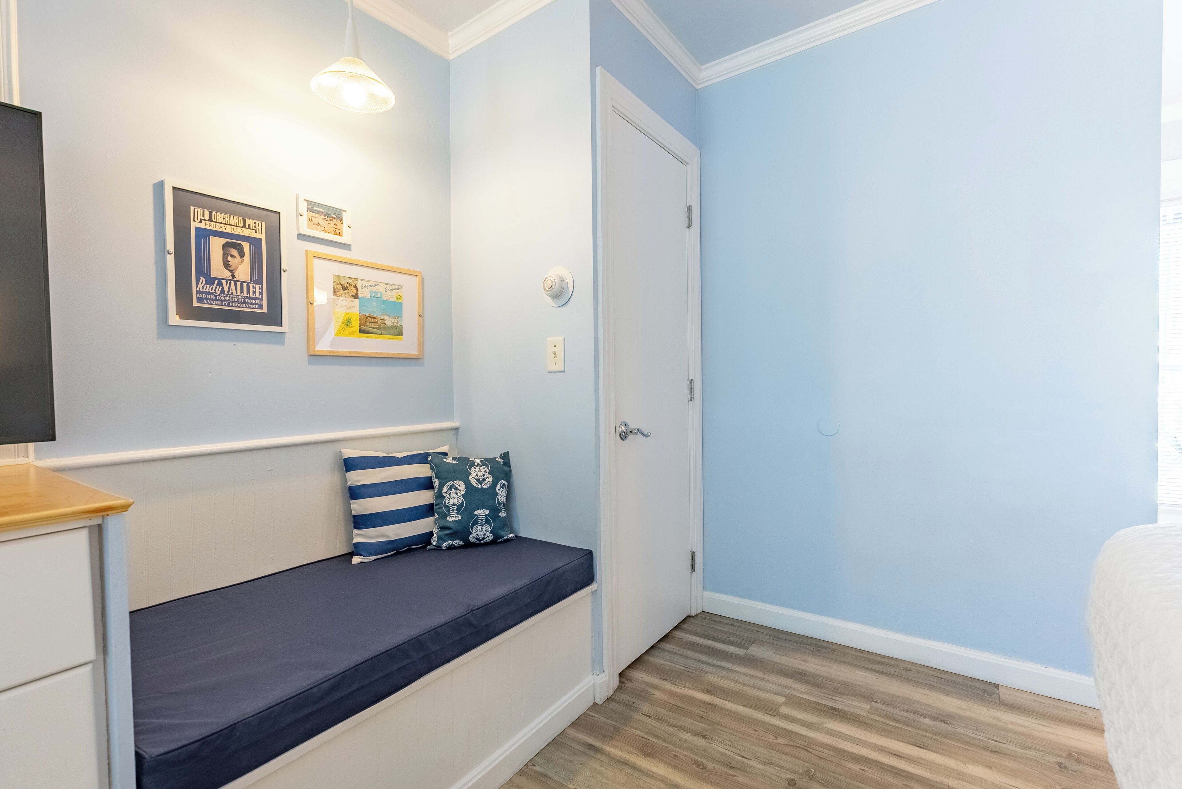 A bedroom with a bed, a bedside table, a wall-mounted TV, and a door.