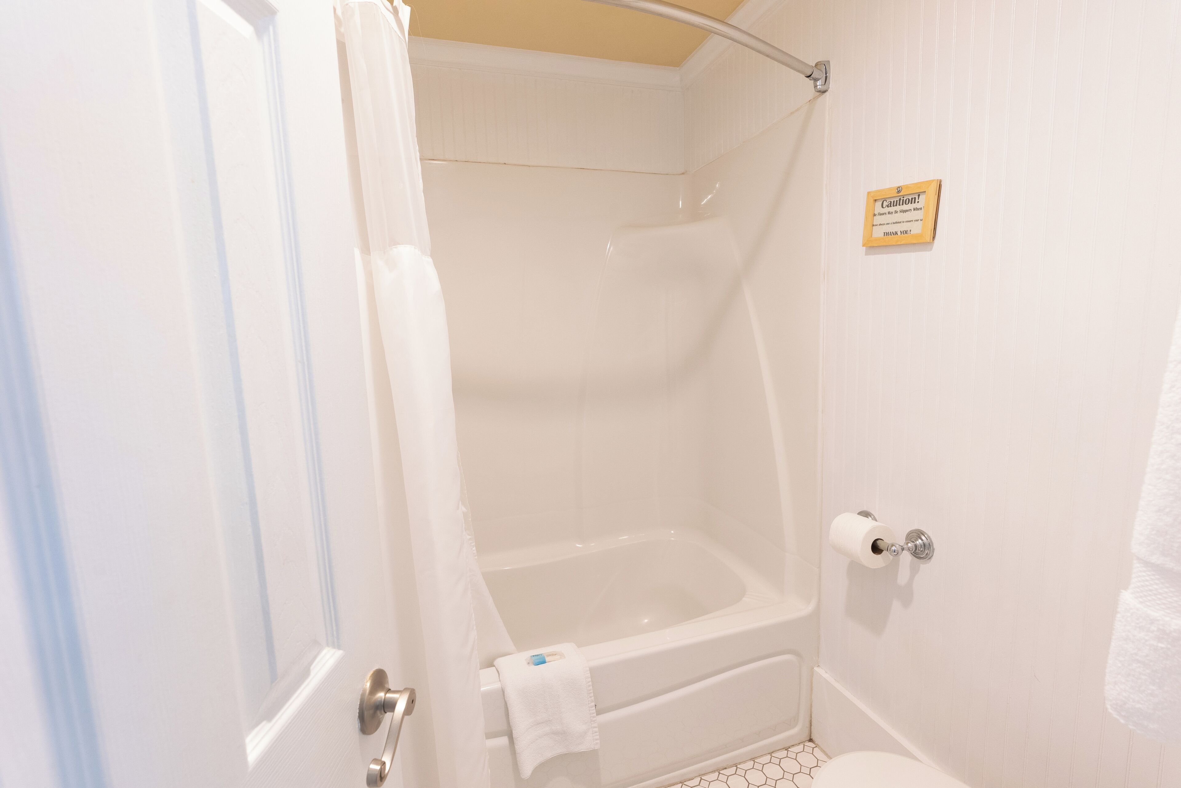 Un baño con bañera, ducha e inodoro. Hay una señal de precaución en la pared.