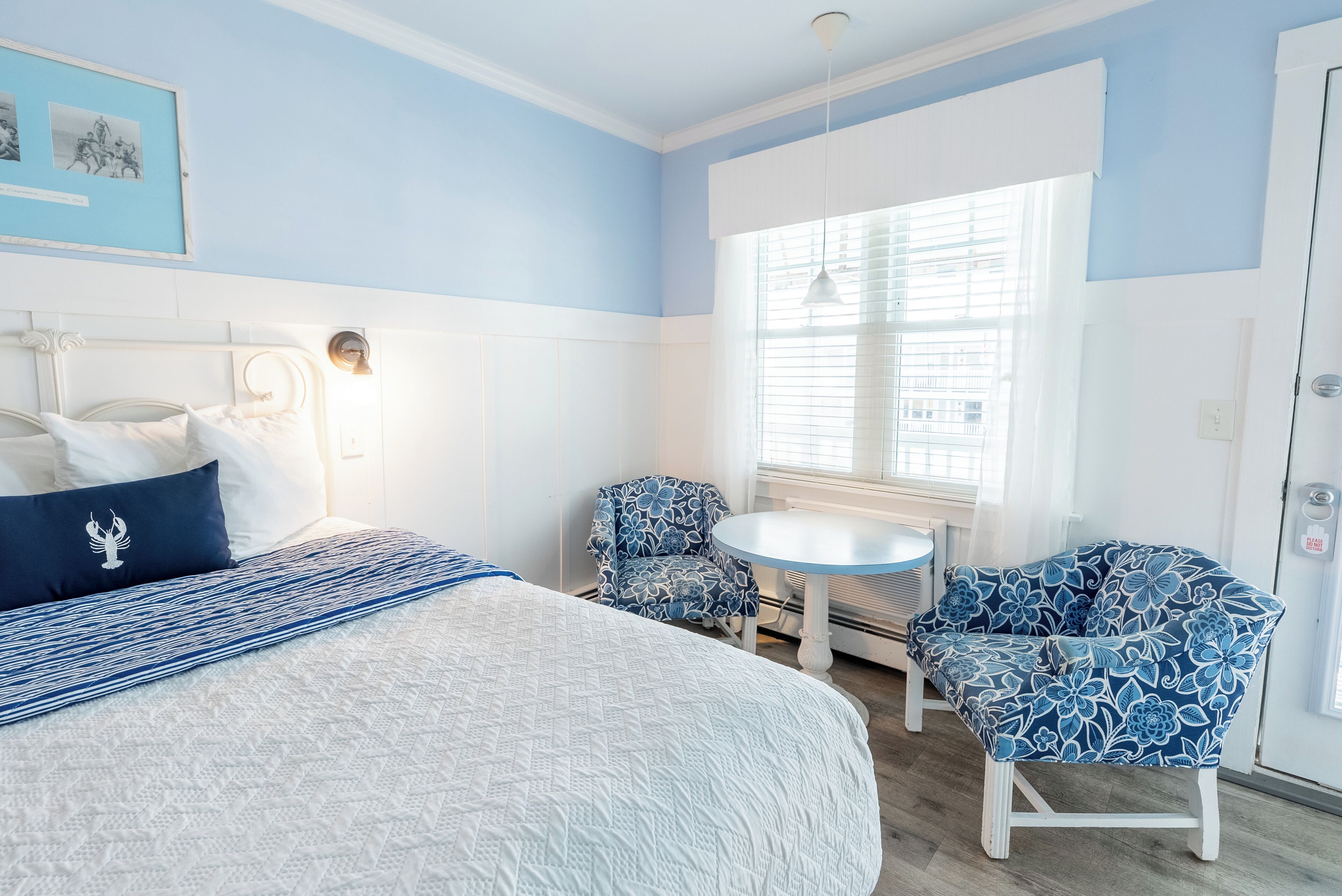 A bedroom with a bed, two chairs, a small table, and a window with blinds.